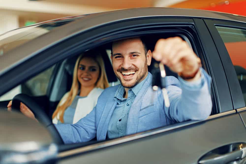 Consultor entregando a chave de um veículo para clientes na concessionária